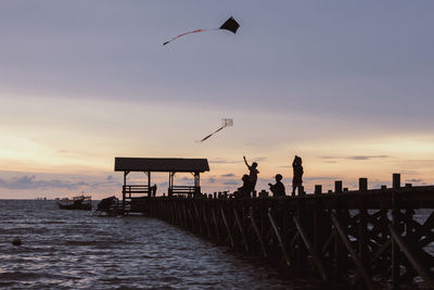 Silhouette of boys flying kite against sky