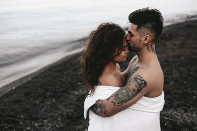 A diverse of lovers a man and a woman embrace under a blanket on the ocean at night outdoor