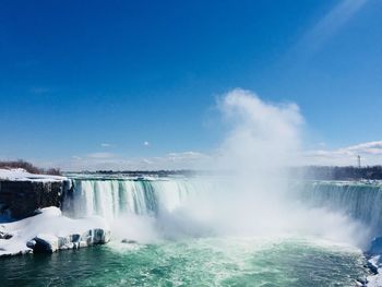 Scenic view of waterfall against blue sky