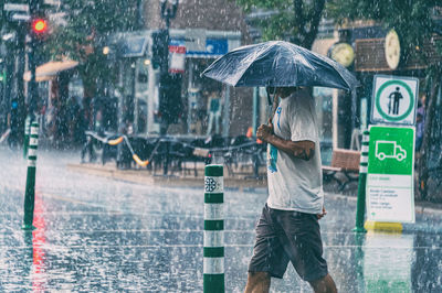 Rear view of woman standing on wet street during rainy season