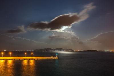 Night view of athens piraeus harbor with moon partially hidden by clouds, greece