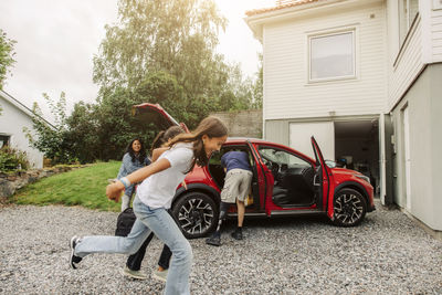 Cheerful daughters playing near electric car by house