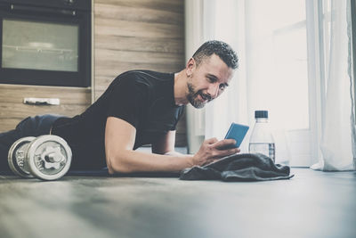 Sporty man resting after working out at home. fit boy looking exercise video lesson on smartphone.