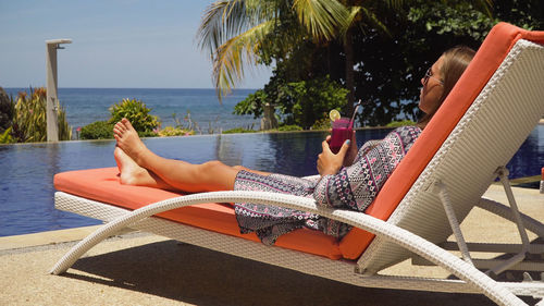 Low section of woman sitting on lounge chair at beach