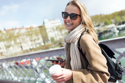 Woman with coffee cup using mobile phone in city