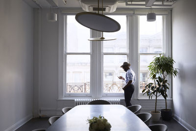 Businessman using mobile phone while standing by window in conference room