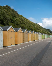 Beach huts on road opposite beach with blue sky