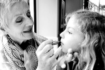 Close-up of grandmother applying lipstick to granddaughter at home