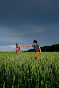 Couple holding hands while standing amidst plants on field against sky