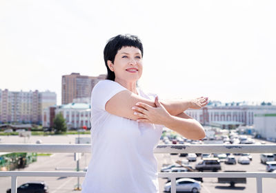 Portrait of smiling young woman in city against sky