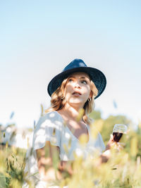  young millennial woman outdoors in apple orchard having a glass of red wine with fedora hat on