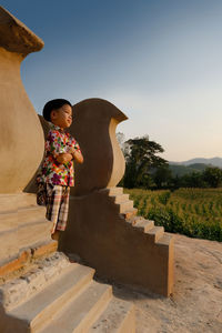 Side view of boy standing on steps against clear sky