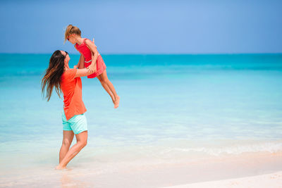 Mother holding daughter at beach against sky