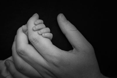 Close-up of baby holding hand against black background