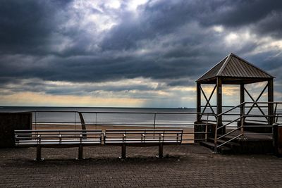 Bench by sea against sky at dusk