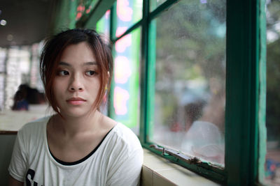 Portrait of beautiful young woman looking through window