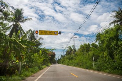 Road sign by trees against sky