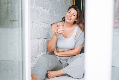 Beautiful young woman plus size body positive in comfortable sport wear with glass of water at home