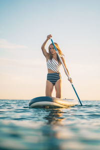 Woman with arms raised in sea against sky