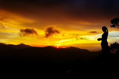 Silhouette man standing on mountain against orange sky