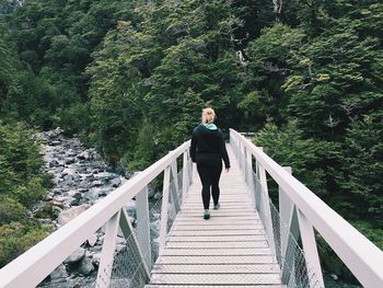 Full length rear view of woman walking on bridge over river in forest