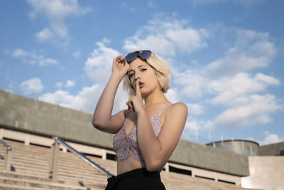 Low angle portrait of young woman with finger on lips against sky