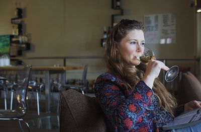 Woman drinking wine while sitting with book at restaurant table