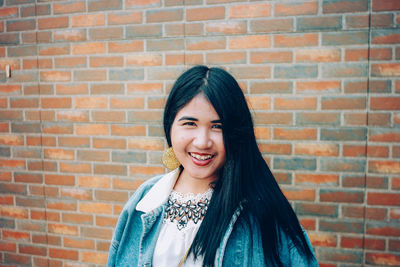 Portrait of smiling young woman standing against brick wall