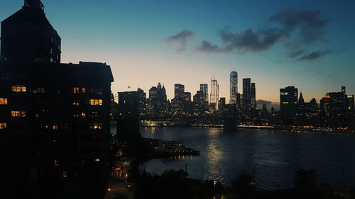 Illuminated city by river at dusk