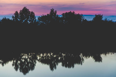 Silhouette trees by lake against sky at sunset