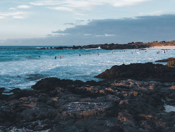 Group of people on rocks by sea against sky