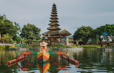 Woman in outrigger at pura ulu danau temple against sky