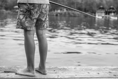 Low section of boy fishing in lake from pier