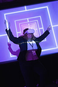 Happy businesswoman wearing vr glasses standing with arms raised in convention center