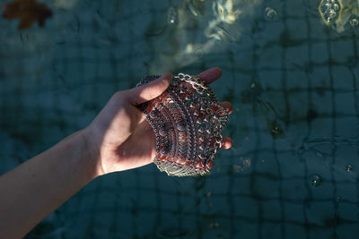 Close-up of hand holding jewelry over swimming pool