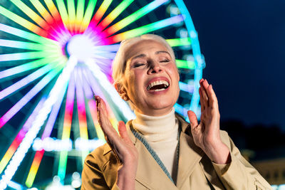 Laughing woman standing against ferris wheel at dusk