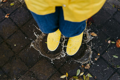 Woman wearing yellow boots jumping on puddle during rainy season