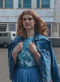 Thoughtful young woman wearing denim jacket while standing against building