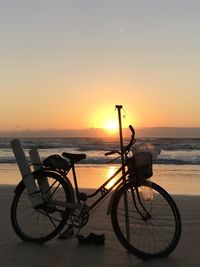 Bicycle on beach against sky during sunset