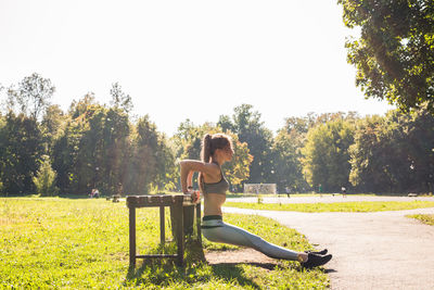 Woman sitting on seat in field against clear sky