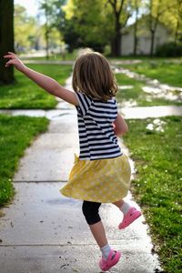 Girl with arms raised running on footpath amidst field at park