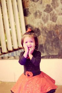 Portrait of smiling girl in dress standing against wall