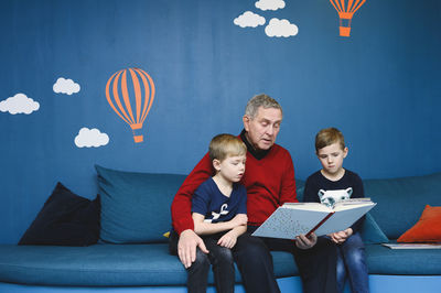 Grandfather reading book to grandsons in library