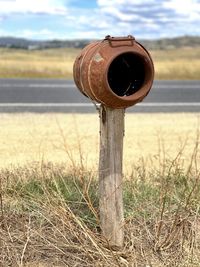 Rusted rural letterbox on field against sky