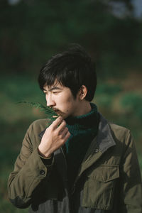 Young man looking away while smelling leaves