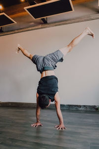 Back view of faceless barefooted man in sportswear standing upside down in downward facing dog pose while training in contemporary gym