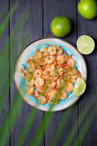 Prawns fried with garlic on a blue porcelain plate with whole and sliced limes on a black table. 