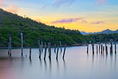 Scenic view of sea with erecting timbers against sky at sunset