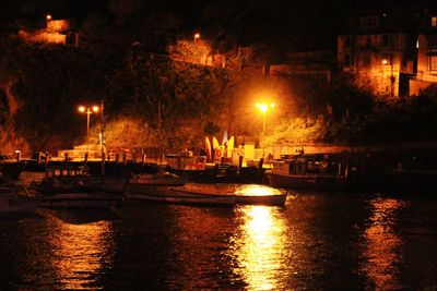 Boats in river against illuminated city at night