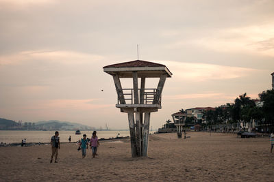 People by lookout tower at beach against sky